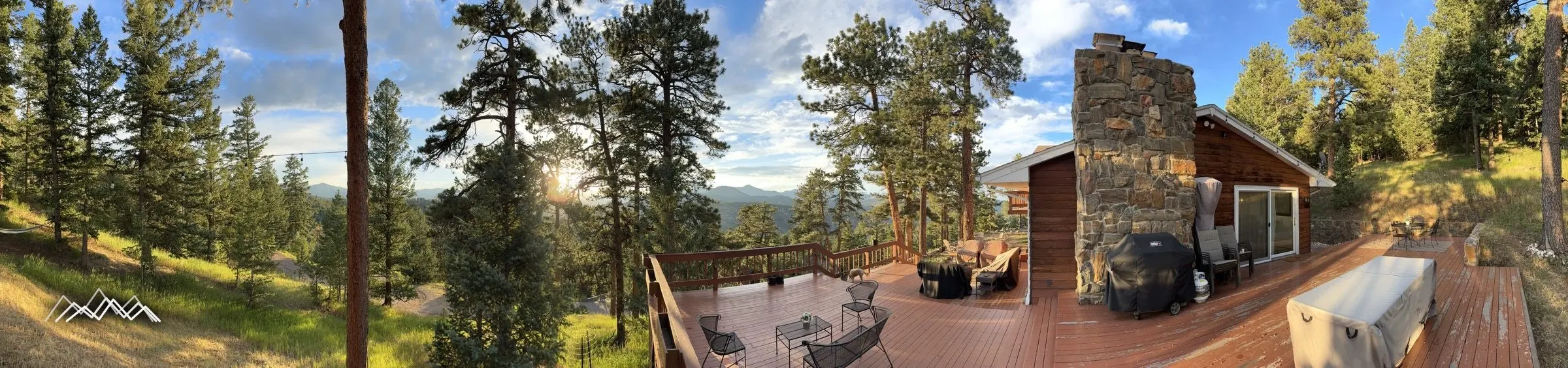 Panoramic view of the full deck, stone chimney, and the mountains at sunset