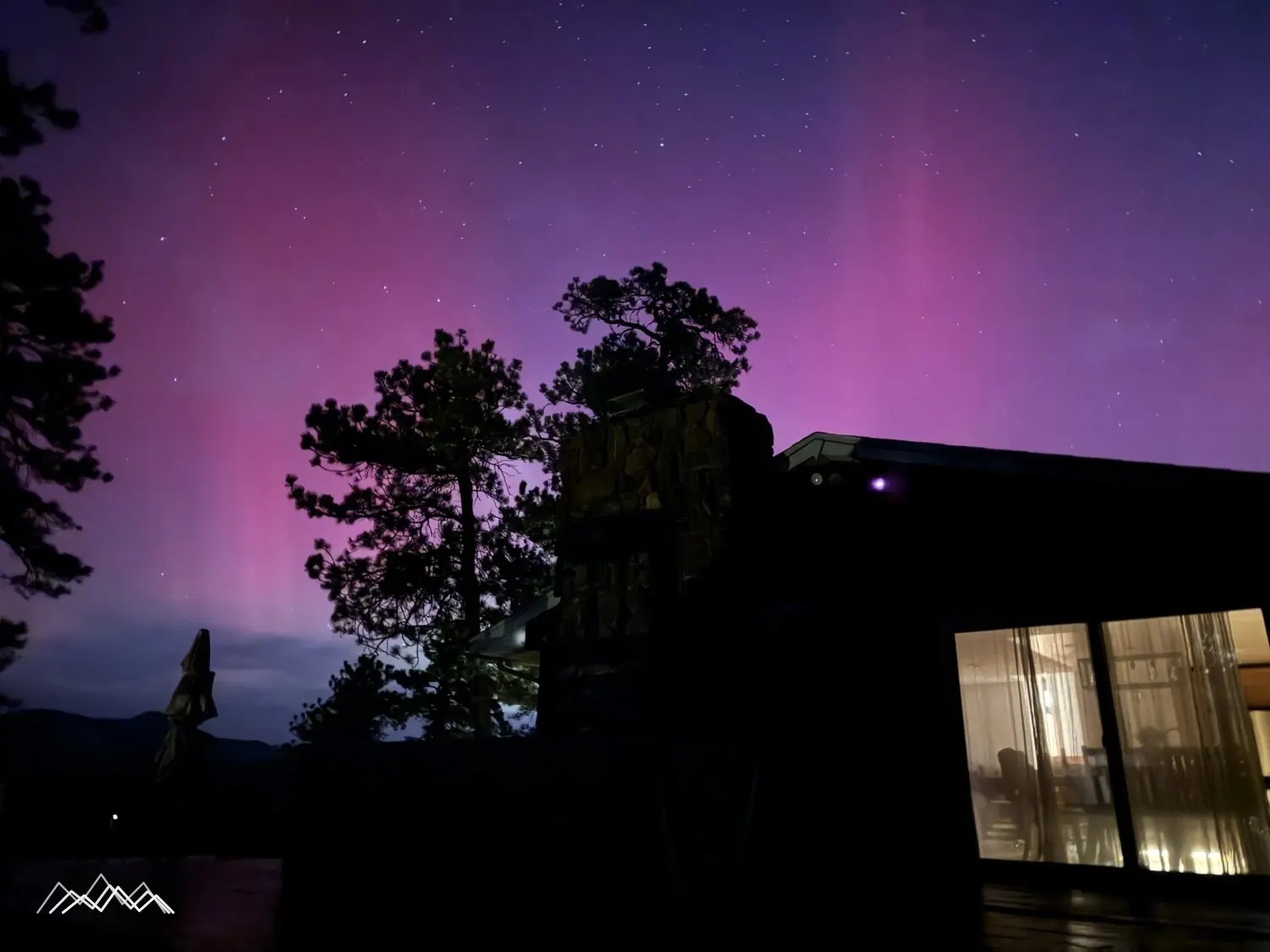 The northern lights above the stone chimney and lit windows of the house