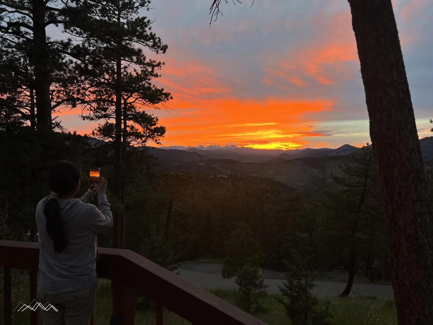 Mily photographing a blazing sunset from the deck railing, silhouetted against the sky