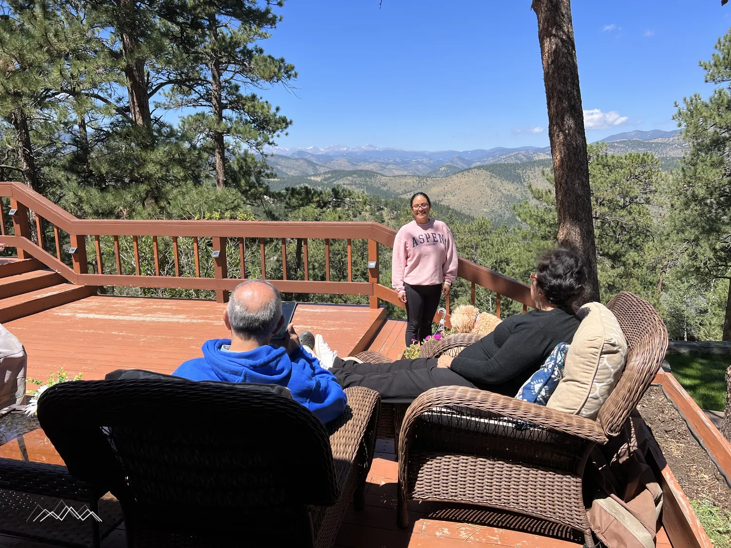 Family relaxing on the deck in wicker chairs on a sunny day, with the mountains beyond the railing