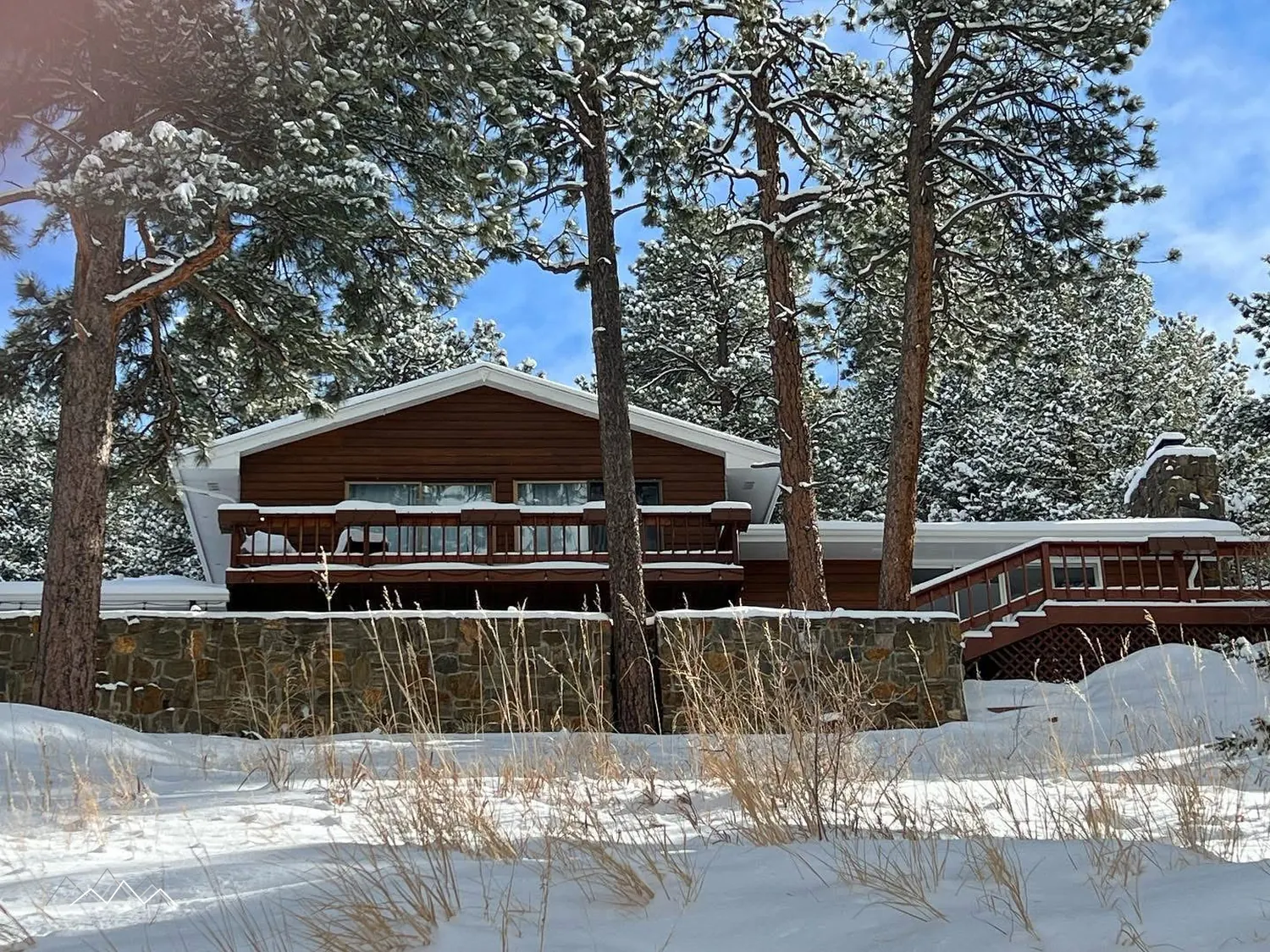 The house, stone wall and ponderosa pines covered in fresh snow under a blue sky