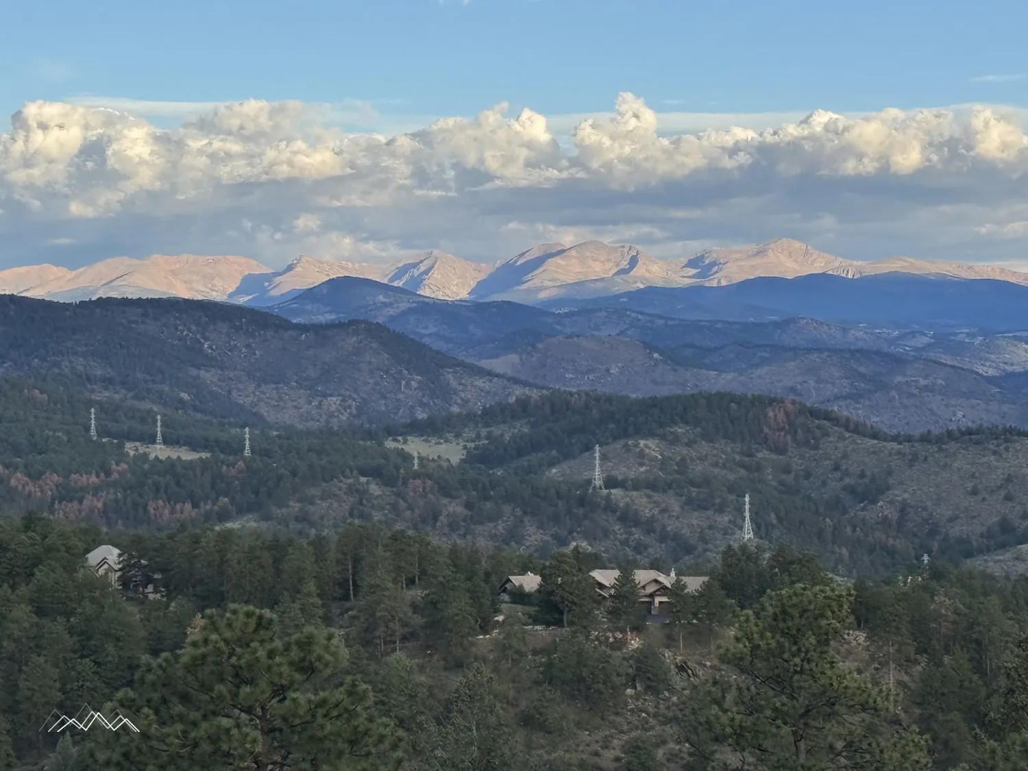 Mountain peaks glowing pink in the early morning light under big clouds, above forested foothills