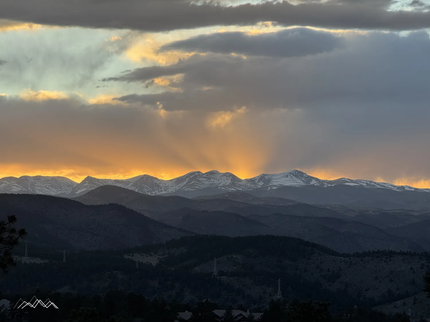 Des rayons du soleil du soir en éventail derrière les Indian Peaks enneigés, sous d’épais nuages